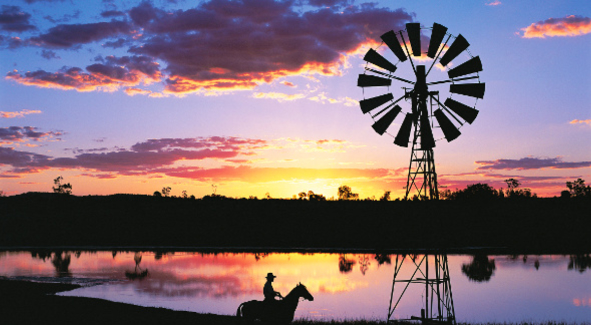 Silhouette of a windmill and a cowboy riding his horse as the sun sets across the lake
