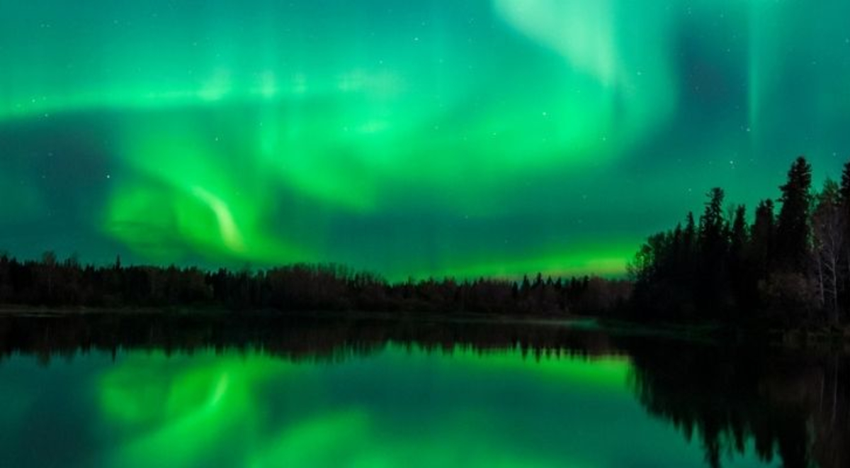 a silhouette of mountains and trees with green northern lights on the background