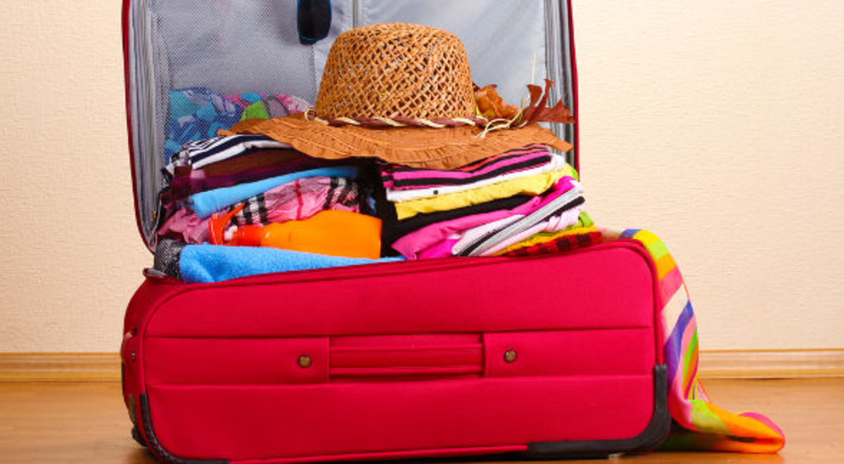 Red luggage full of colorful clothes and a hat