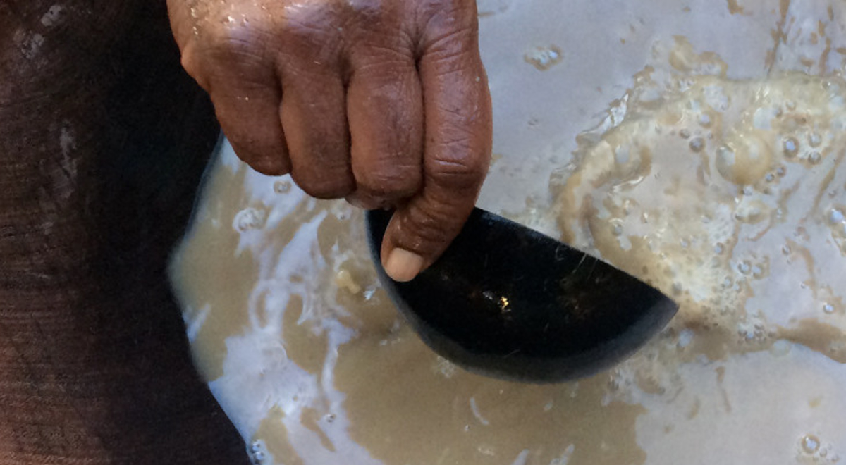 a person scooping kava out of a wooden pot