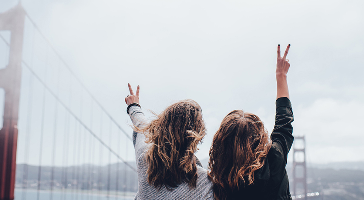 two female friend holding up a peace sign while looking at the bridge