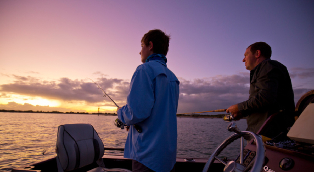 Two men fishing on a boat as the sun sets