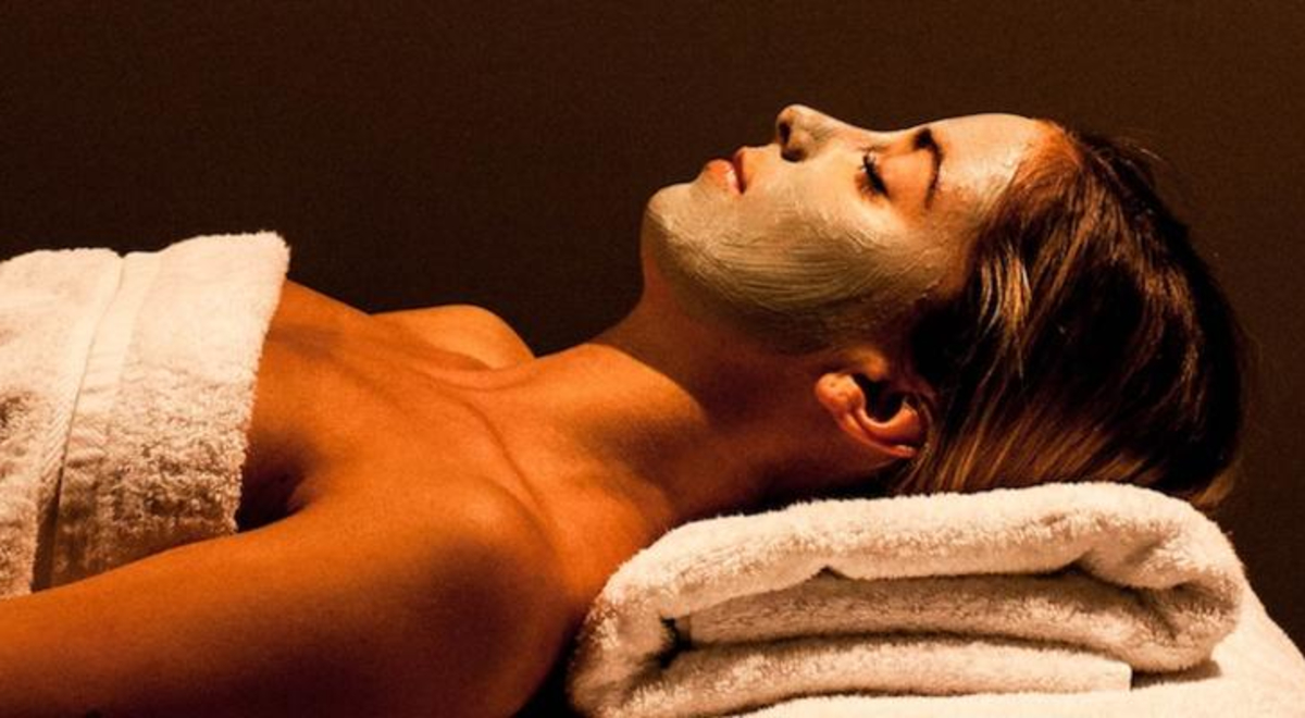 a woman wrapped in a white towel relaxing on a spa bed with a facial mask
