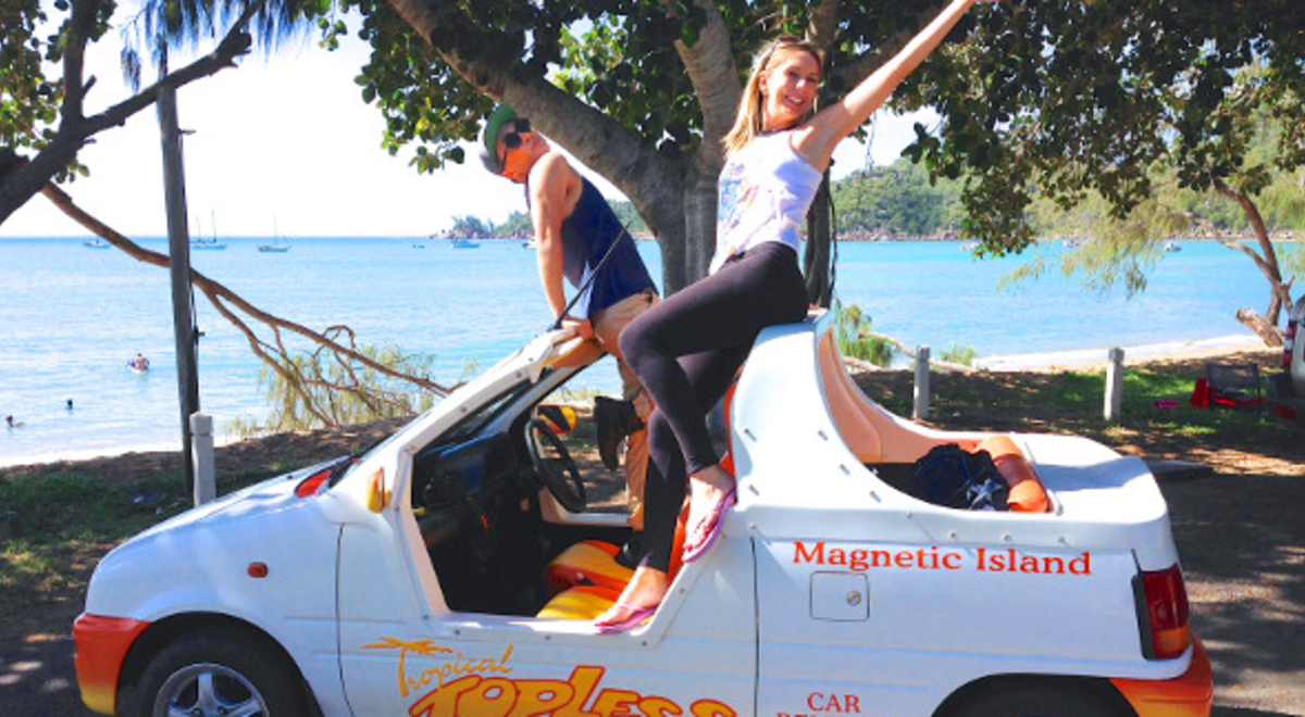 Couple posing on top of a rental car near the beach
