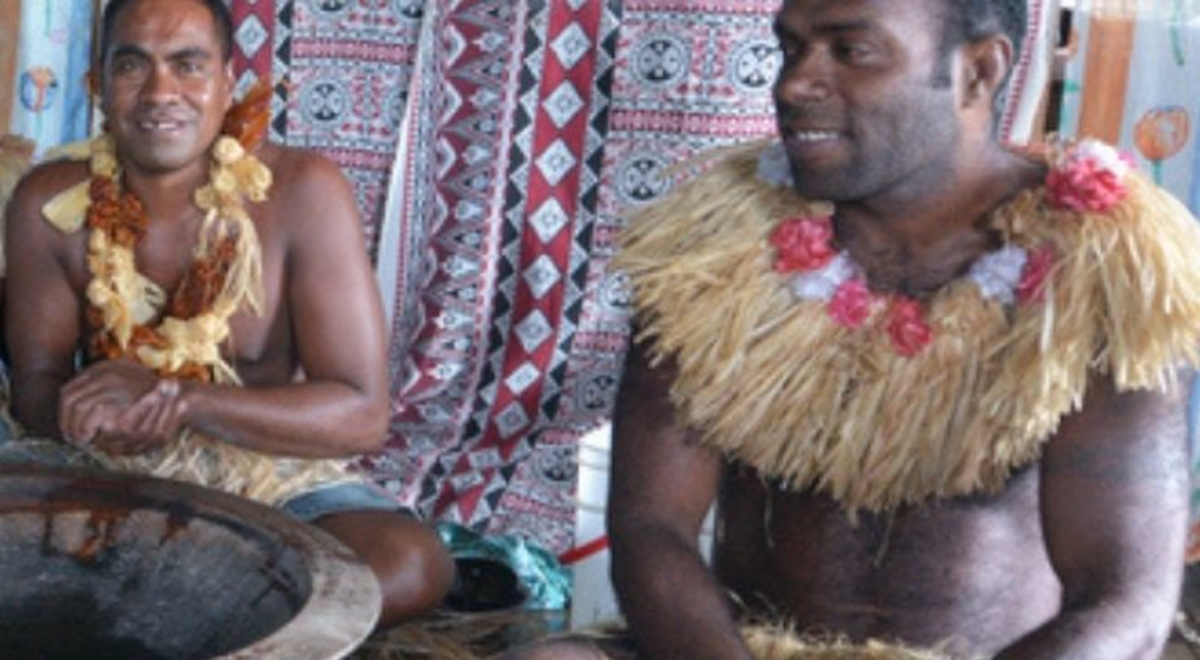 Fijian men sitting on straw mat with bowl of kava in front 