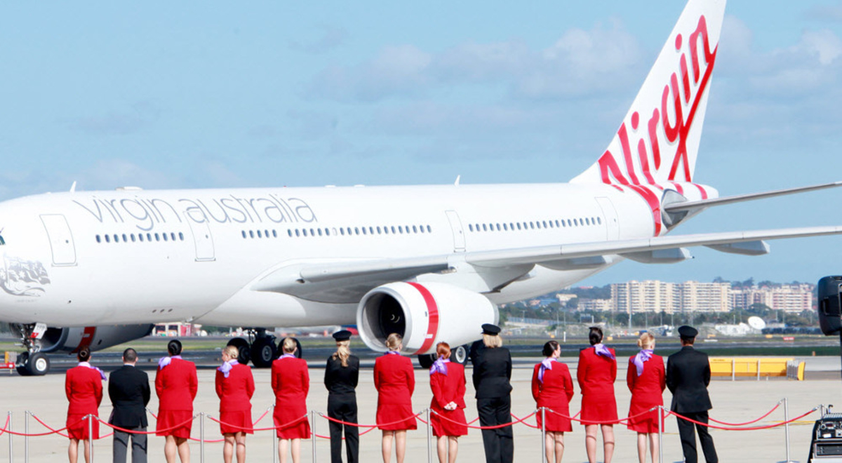 Flight crew standing on a red carpet on the runway looking at a Virgin Australia airplane