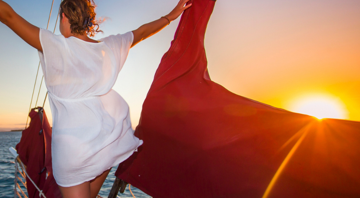 a girl in white dress standing on the edge of the boat admiring the beauty of the sea during sunset