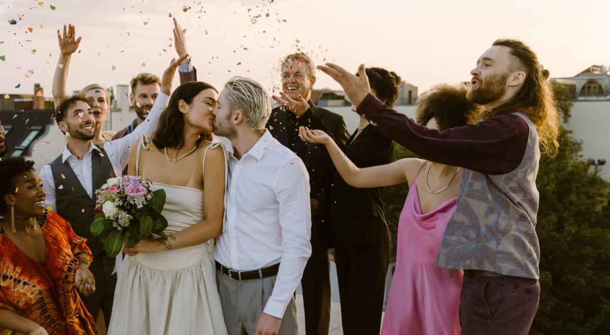 Guests throwing confetti as wedding couple kisses