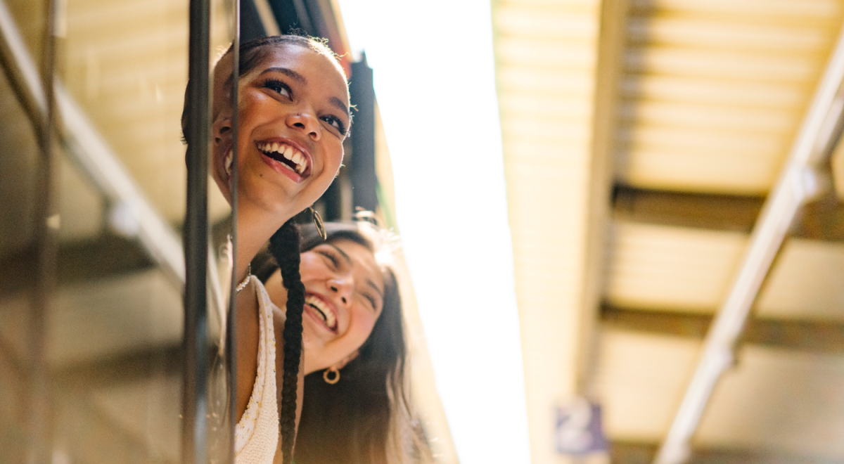 Two women aboard a train; they're looking out of its doors while stopped at a platform