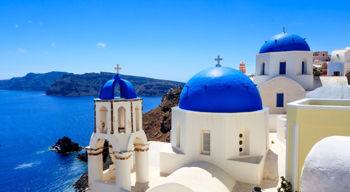 Looking over the blue domes of Santorini, Greece with a blue sea, blue sky and a large island on the horizon 