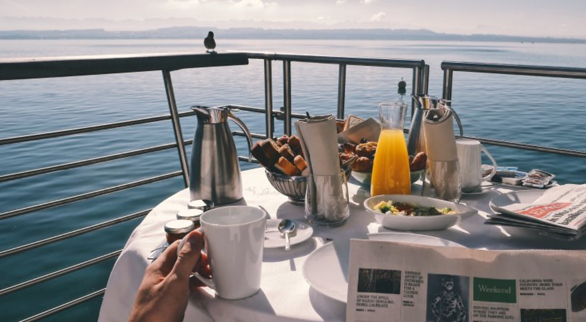 Table set for breakfast on luxury yacht with person reading newspaper in forground