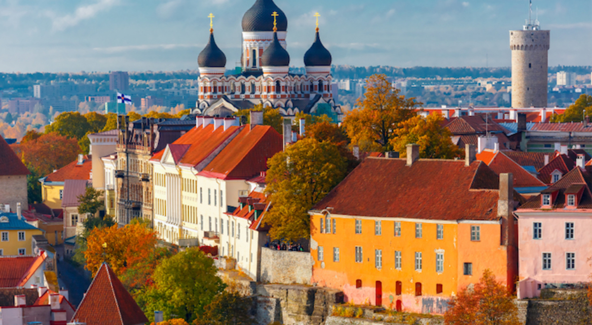 A blue onion-domed church sits among large red-roofed housing block on a hill overlooking the town in the background