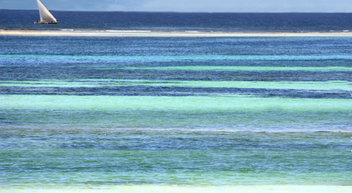 Different shades of blue ocean water with a small sail boat in the background