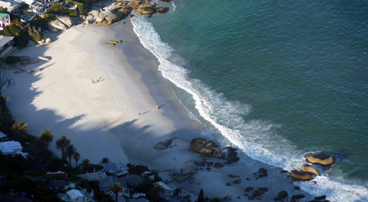 A drone's view of a suburban bay with a sandy beach and rocks.
