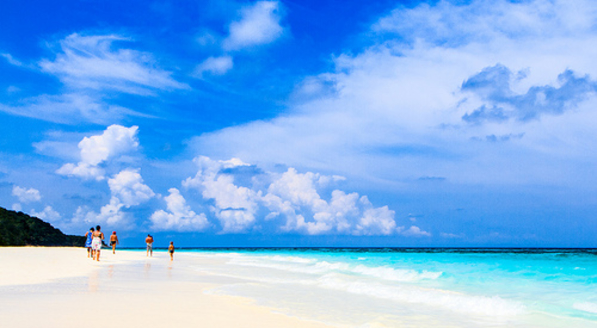 A family walks along a white sandy beach by an azure lagoon