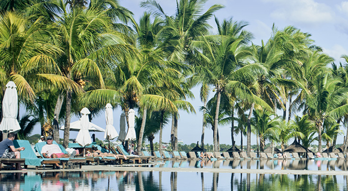 A person in a white flowing dress walking across a bridge between two pools at a tropical destination