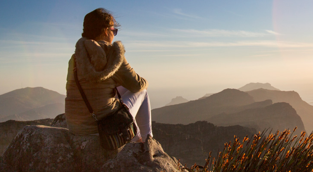 Middle aged woman sitting on a ledge looking at the view from the top of the mountain
