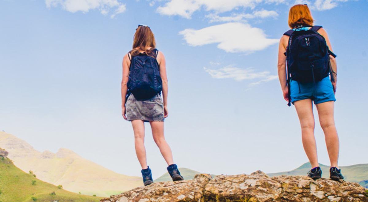 Two female presenting people stand on a rock looking at a mountain in The drakensberg south Africa 