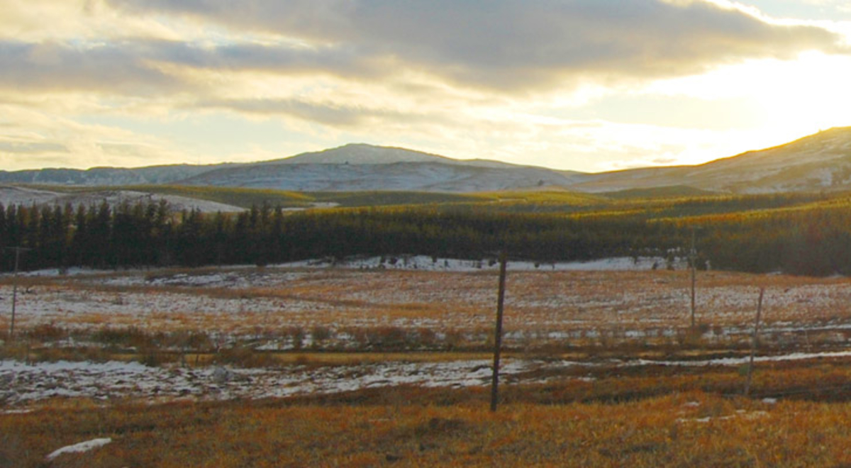 The sun rises behind hills and grassland covered in snow