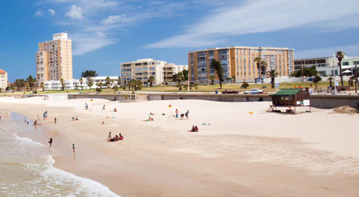 People swim and bathe on a beach with hotels in the background.