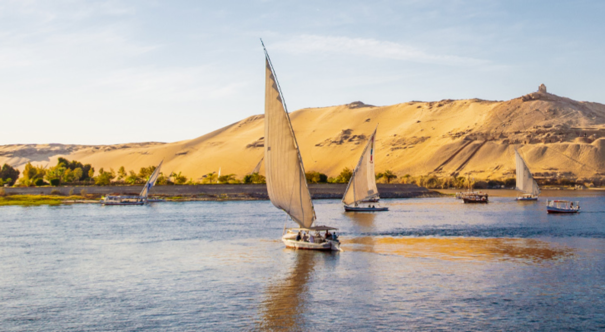 Sail boats floating on a river with a green hillside in the background