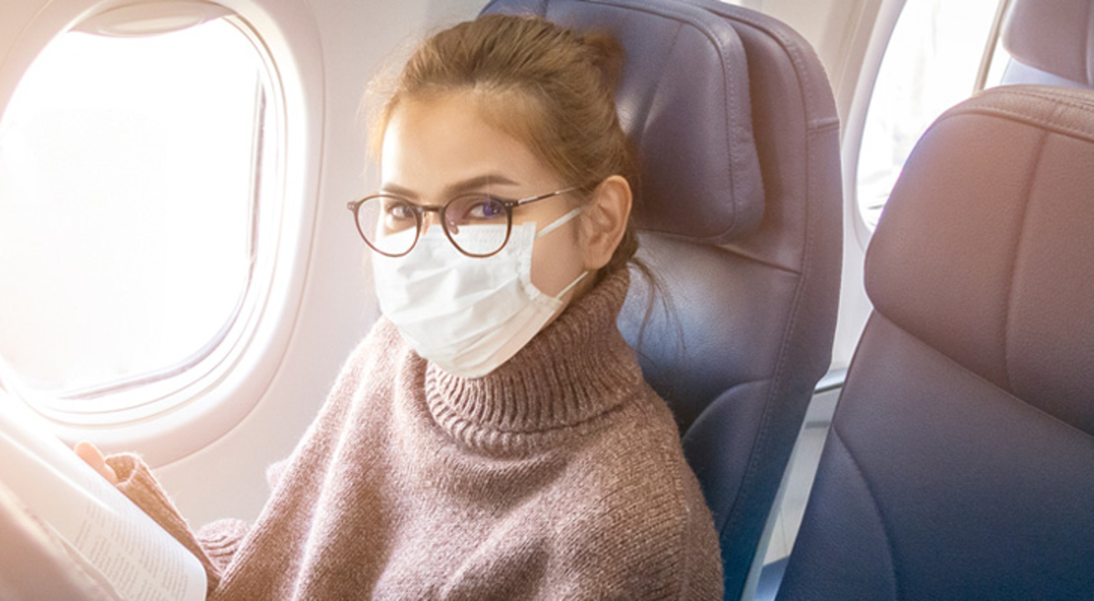 Lady sitting on a plane wearing a brown turtleneck with a mask and glasses 
