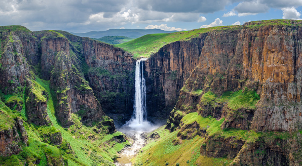 A waterfall falls from cliffs coloured green and brown in Lesotho Africa