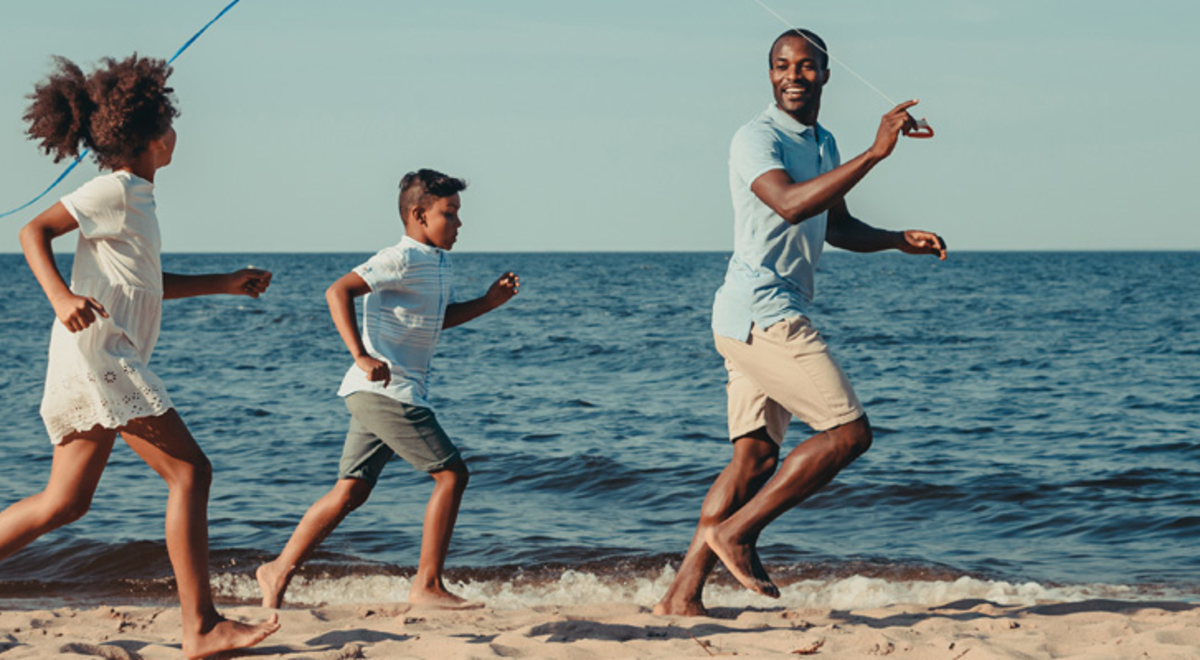 one male presenting adult and two children run on sand of beach with ocean in background