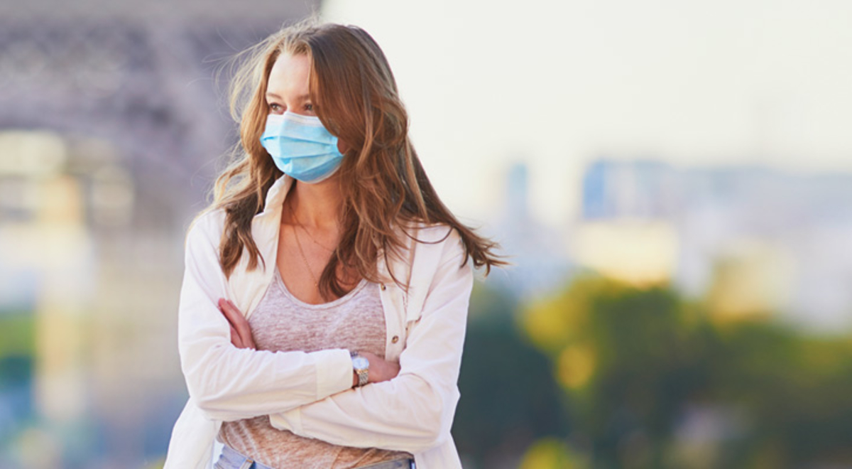 A person wearing a mask standing in front of the Eiffel Tower