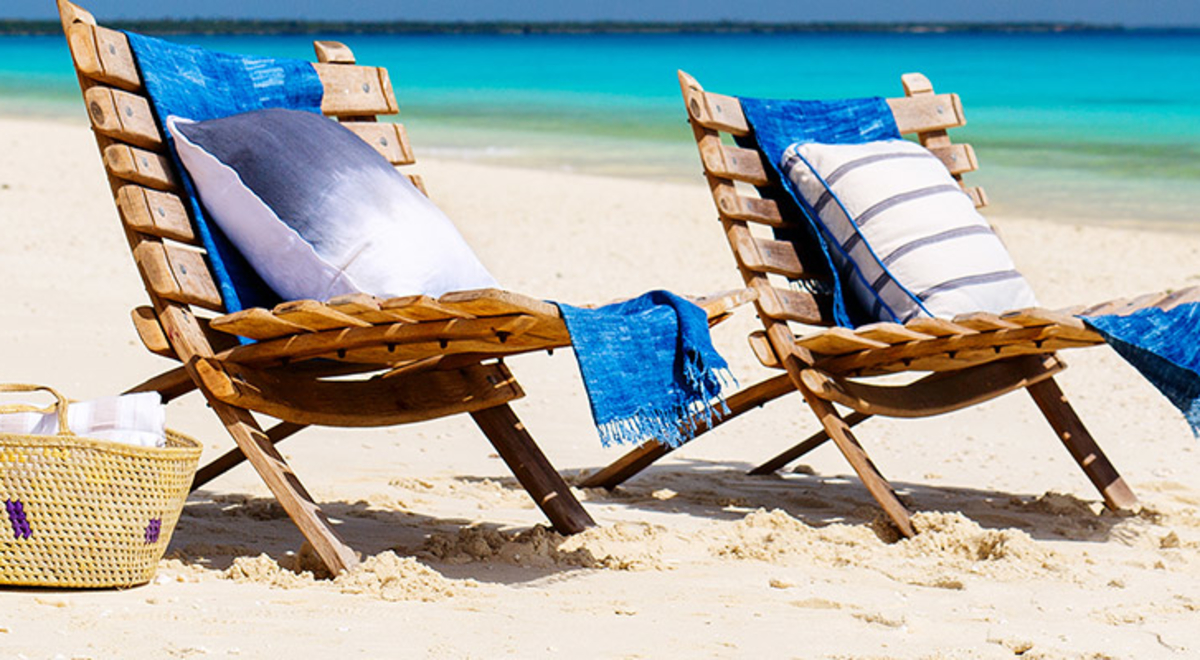 beach chairs with towels and cushions and picnic basket sitting on white sands of the beach with blue ocean in background 