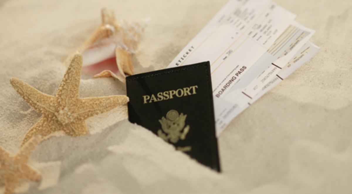 Passport and plane tickets next to starfish on the sand 