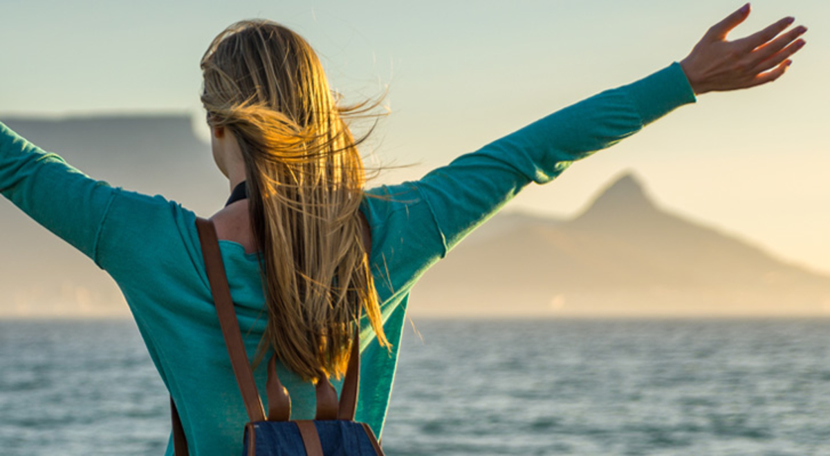 A woman stands with her arms stretched on the beach with a view of Table Mountain in Cape Town, which can be visited with a cheap holiday package from Flight Centre.