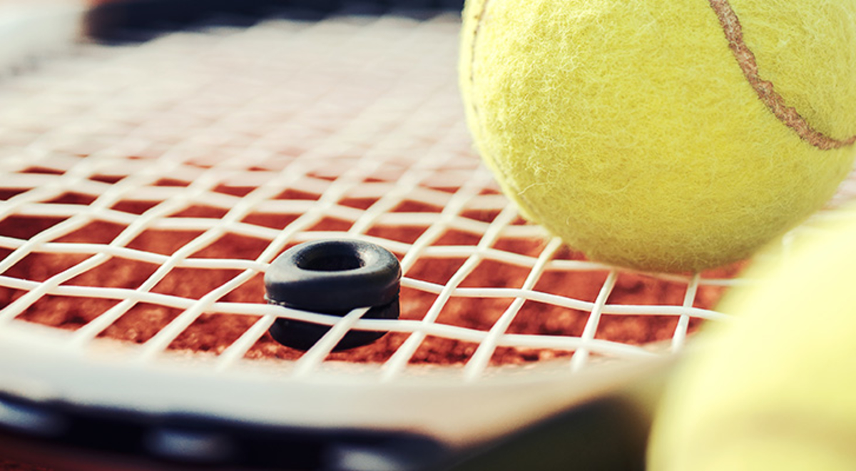 Tennis balls sitting on and next to a tennis racquet