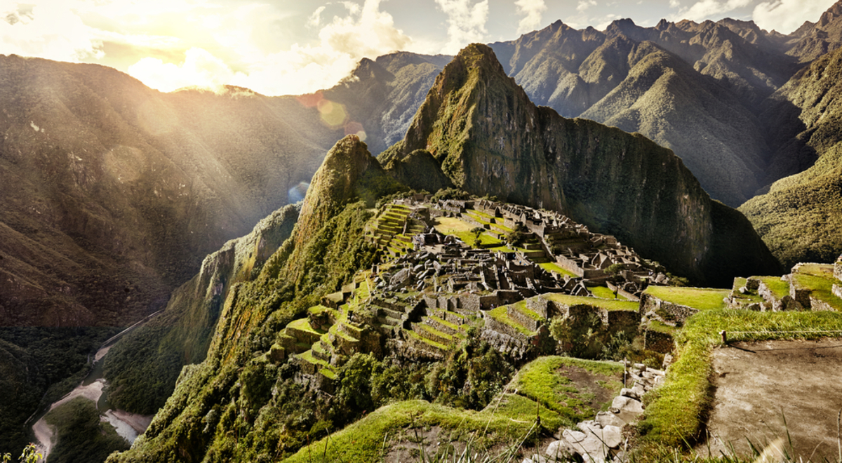 ruined buildings sitting on top of a mountain as the sun rises over the mountain range