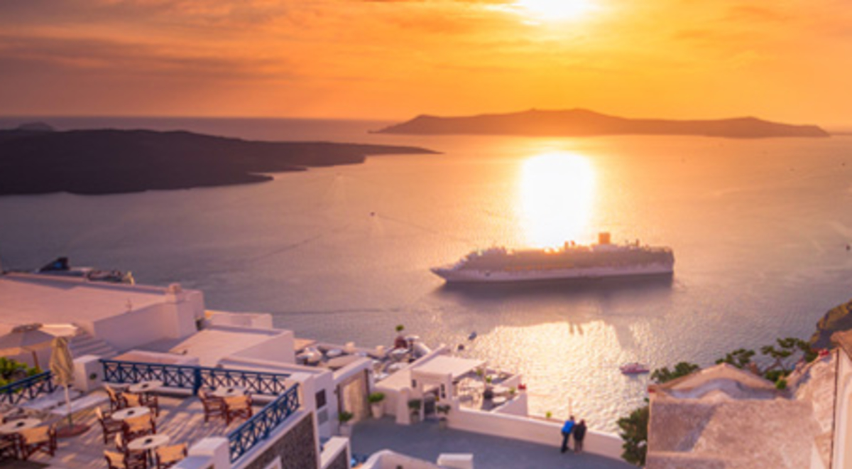 A cruise ship sails to shore in a bay below Santorini, Greece at sunset