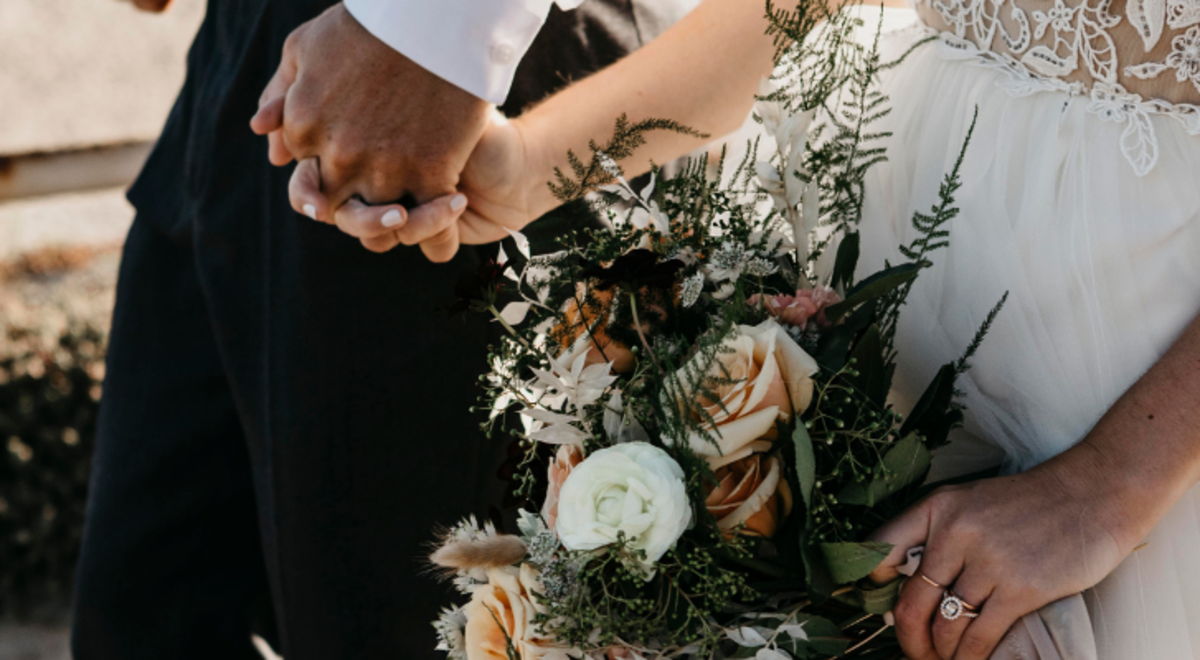 A close up of a bride and groom holding hands