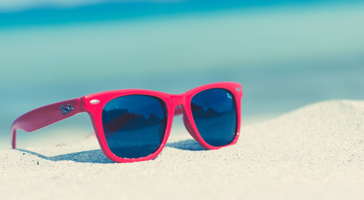 A pair of red sunglasses sitting on a white sand beach