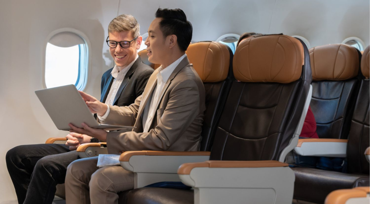 Two men sitting in business class on a plane looking at a laptop together