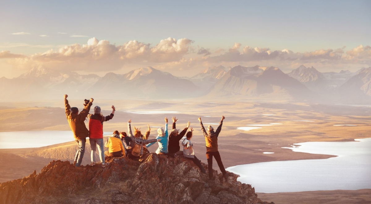 group of friends standing on top of mountain with arms up