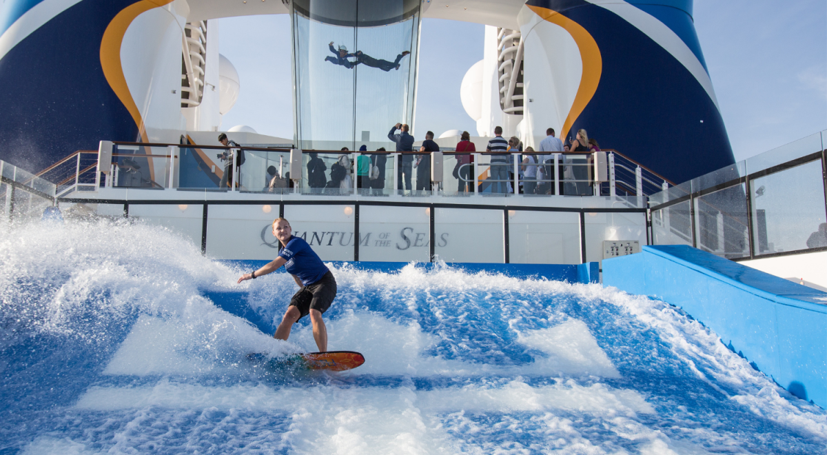 A woman rides the Surf-rider with two people in a skydiving simulator onboard a cruise ship