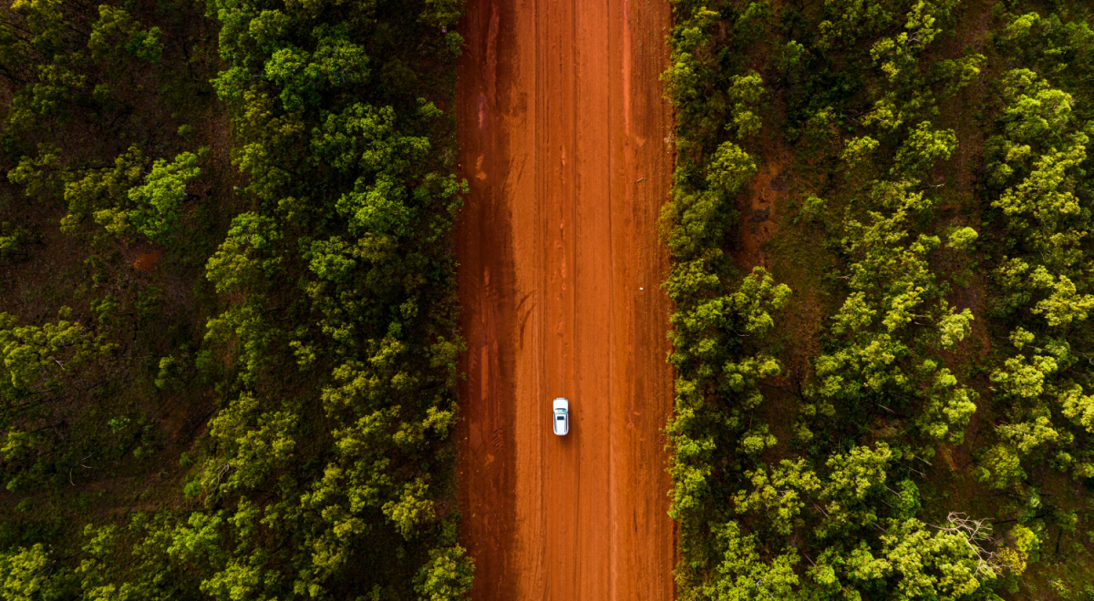 White car driving down a red dirt road in the Australian Outback