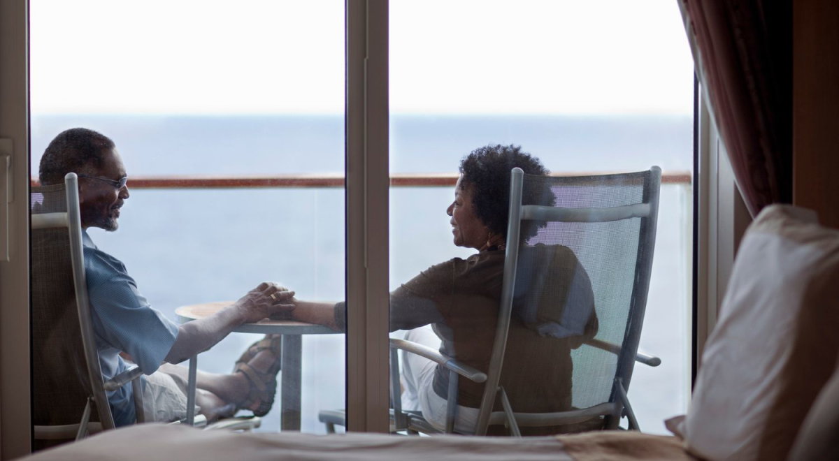 couple sitting on chairs and holding hands on balcony of cruise ship room 