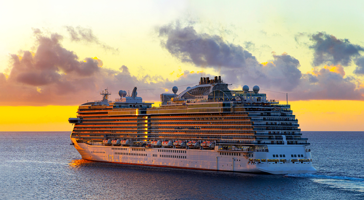 A cruise ship on the ocean with the sun setting in the background