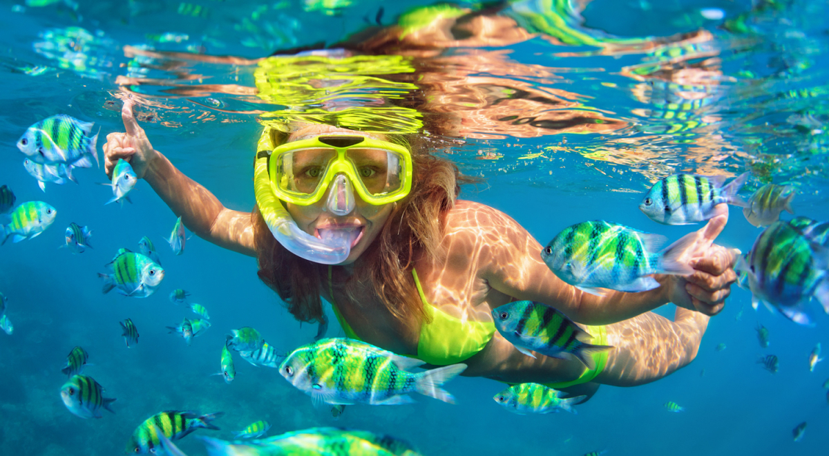 A woman wearing a yellow snorkel mask surrounded by a school of fish