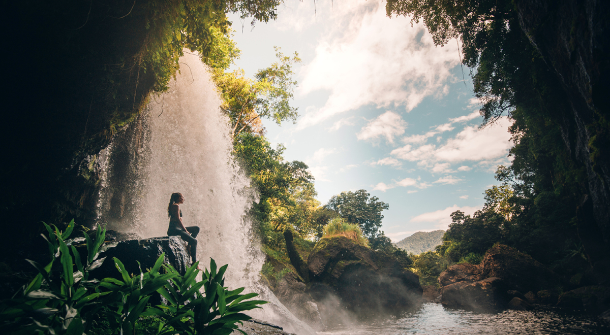 A woman sitting behind Millaa Millaa Falls in Queensland, Australia