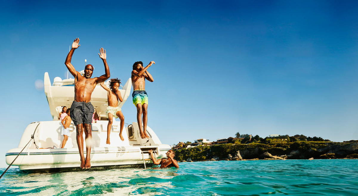 A dad and two kids jumping off the back of a boat into turquoise waters while on a family vacation