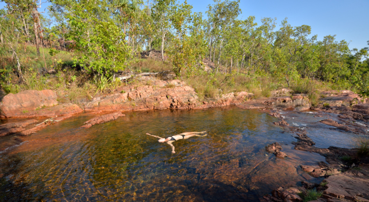 A woman in a black bikini floats on her back in the clear waters of a rock pool in Litchfield National Park in the Northern Territory Australia
