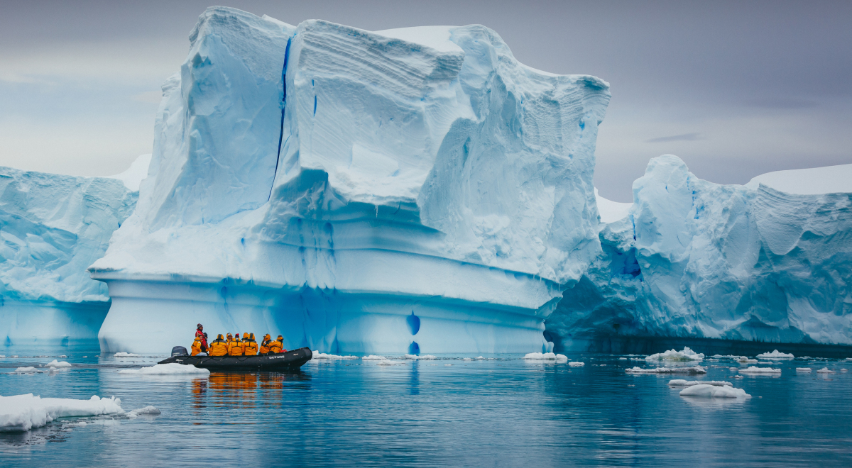 A small boat full of people sailing past an iceberg