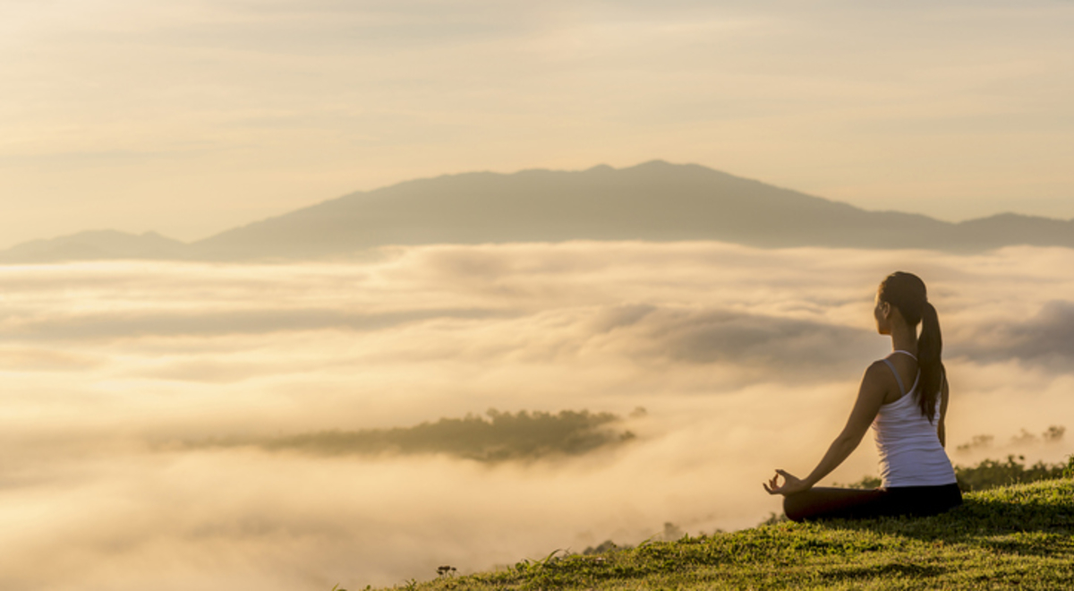 Side view of woman meditating while sitting on field by cloudscape