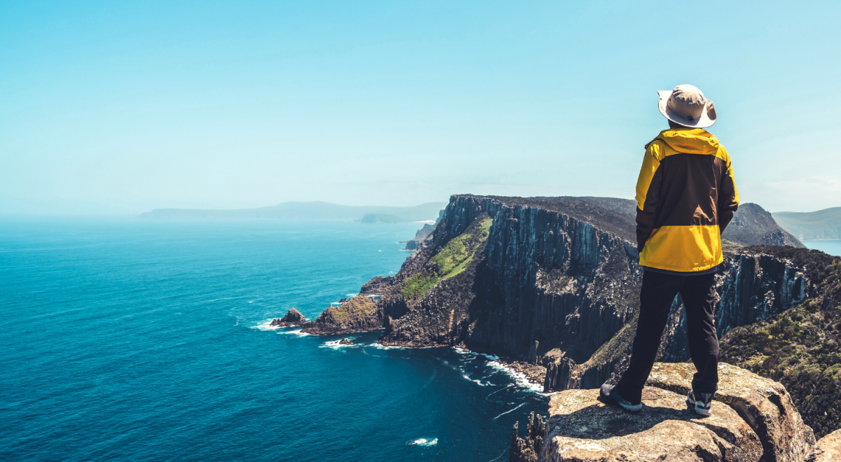 Traveller in a yellow jacket looking out over cliffs by the ocean